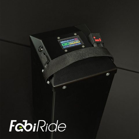 Juodas elektrinis krosinis motociklas su geltonais akcentais žalios sienos fone.