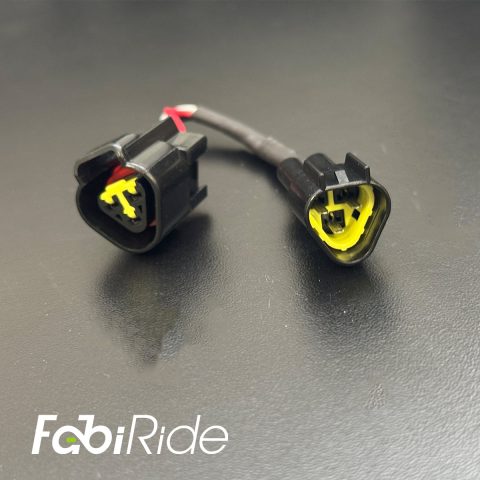Elektrinio motociklo laidų adapteris su dviem juodomis jungtimis ir geltonais vidiniais kontaktais „FabiRide“ fone.